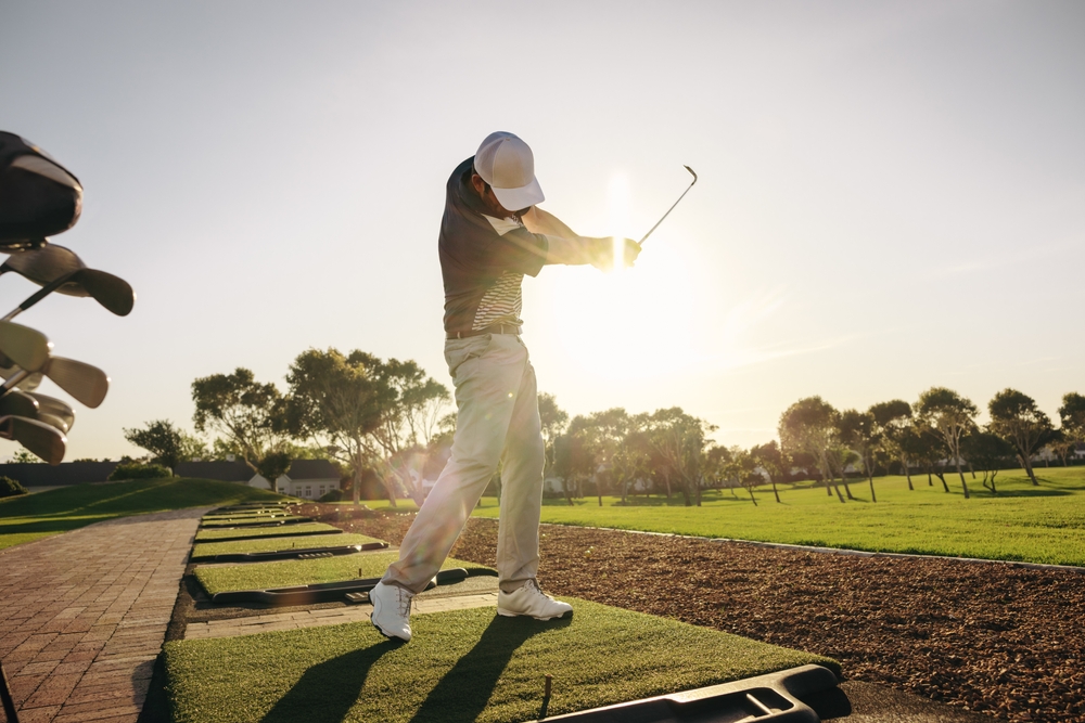 Saisi en plein élan puissant, un golfeur professionnel s’entraîne sous un soleil éclatant sur un parcours de golf paisible. Homme frappant un coup au practice de golf.