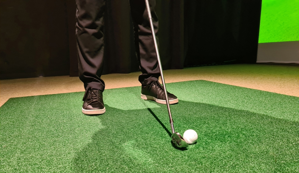 Male golfer plays golf indoors on golf simulator closeup. Driving range with screen