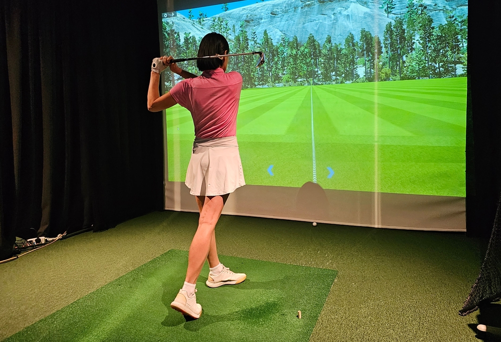 Indoor golf practice session featuring a female golfer using a simulator in a woodland setting